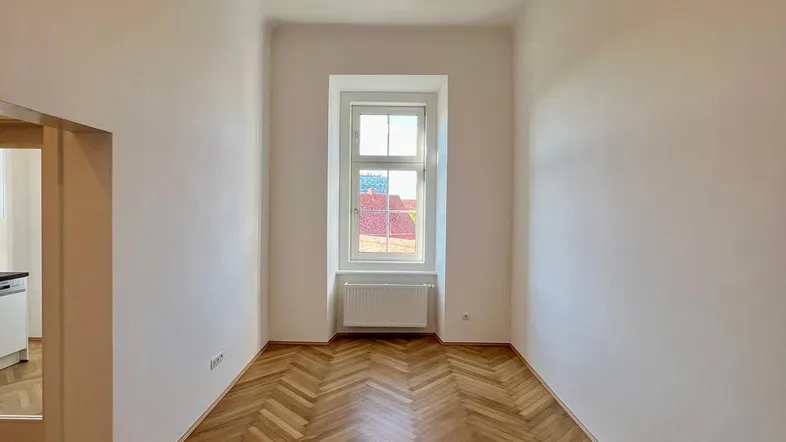Helles Zimmer mit Fischgrätparkettboden und weiß gestrichenen Wänden, bereit zum Einzug.