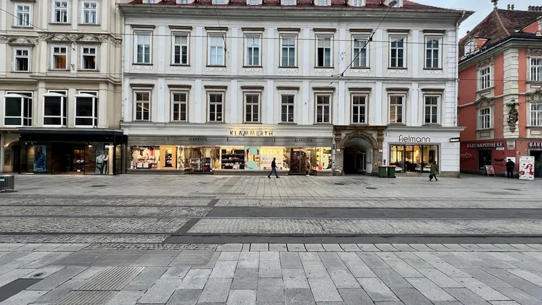 Historisches Gebäude mit Geschäften im Erdgeschoss und Wohnungen darüber an einem belebten Stadtplatz.