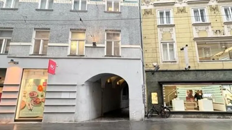 Historische Gebäudefronten mit Geschäften im Erdgeschoss und einem Durchgang zur Straße.
