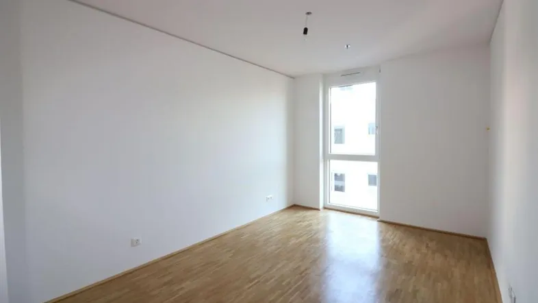 Helles, leeres Zimmer mit Holzboden und großem Fenster, bereit zur individuellen Gestaltung.