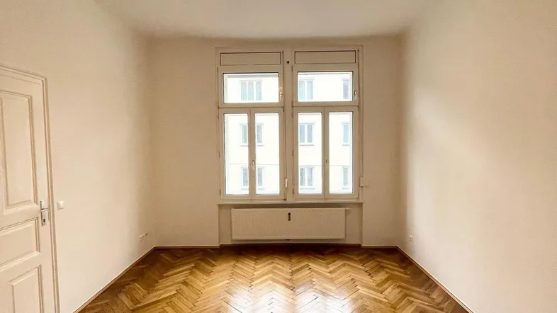 Helles Zimmer mit Fischgrätparkettboden und großen Fenstern, ideal als Wohn- oder Schlafzimmer nutzbar.