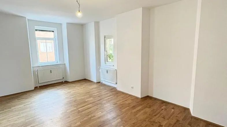 Helles Zimmer mit Parkettboden und zwei Fenstern, ideal als Wohn- oder Schlafzimmer nutzbar.