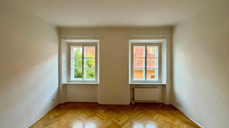 Heller Raum mit Fischgrätparkettboden und zwei Fenstern, die viel Tageslicht hereinlassen.