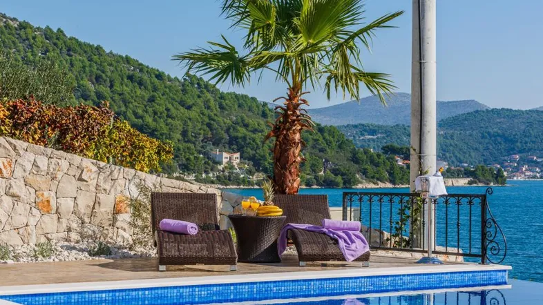 Entspannungsbereich am Pool mit Liegestühlen, Palmen und herrlichem Meerblick unter blauem Himmel.