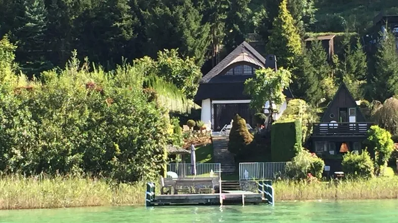 Malerisches Haus am Seeufer mit eigenem Steg, umgeben von üppiger Vegetation und Wald.