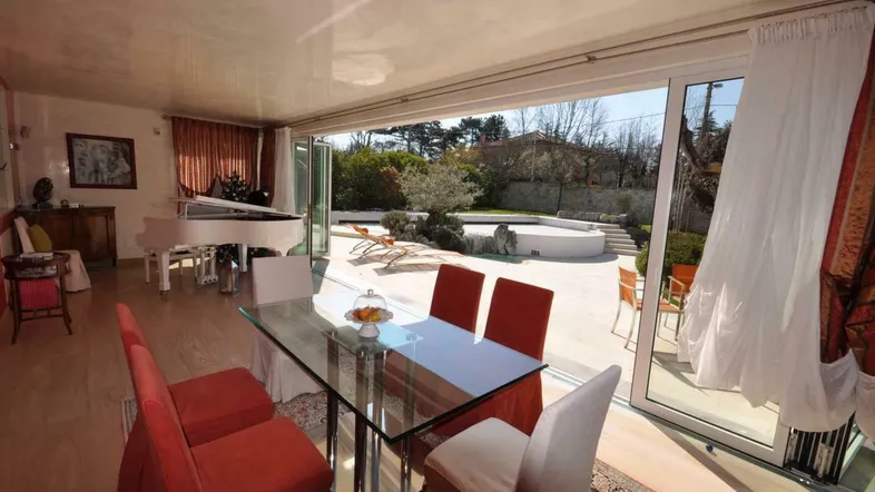 Heller Wohn- und Essbereich mit Glastisch, Flügel und direktem Zugang zur Terrasse und zum Poolbereich.