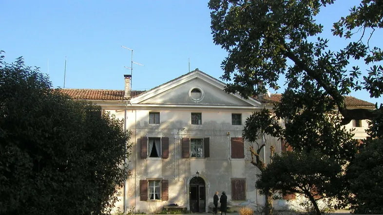 Altes Herrenhaus mit klassischer Fassade, braunen Fensterläden und umgebenden Bäumen.