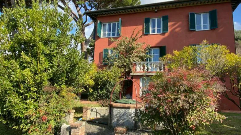 Rotes Haus mit grünen Fensterläden und einem gepflegten Gartenbereich mit Brunnen.