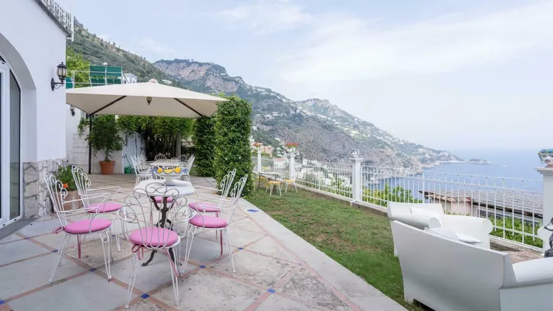 Geräumige Terrasse mit Essbereich, Sonnenschirm und weitem Blick auf die Küste und das Meer.