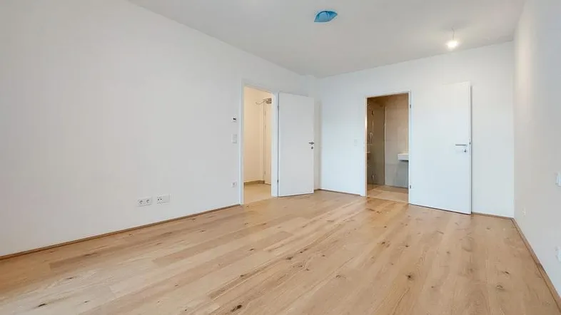 Heller, leerer Raum mit neuem Holzparkettboden und weißen Wänden, mit Zugang zu einem modernen Badezimmer.