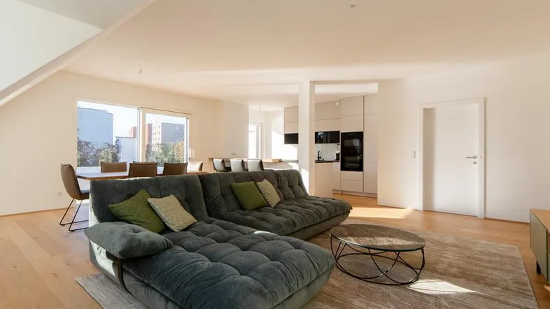 Helles, offenes Wohn-Esszimmer mit bequemer Couch, Holzboden und Blick auf den Essbereich und die Küche.