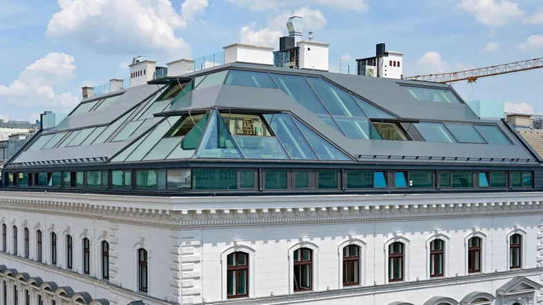 Modernes Dachgeschoss mit Glasdachkonstruktion auf einem historischen Gebäude unter blauem Himmel.