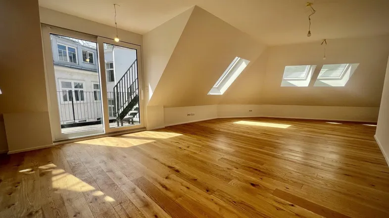 Heller Dachgeschossraum mit Holzboden, Dachfenstern und Zugang zu einer Außenterrasse.