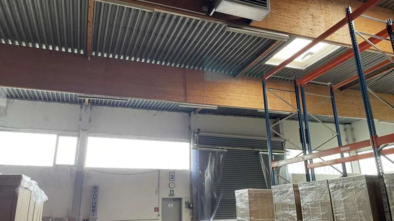 Geräumige Lagerhalle mit hohen Decken, sichtbaren Holzbalken und natürlichem Lichteinfall durch Fenster und Oberlicht.