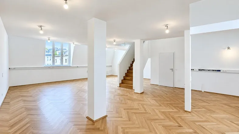 Geräumiger, heller Büroraum mit Fischgrätparkett, hohen Decken und großen Fenstern.