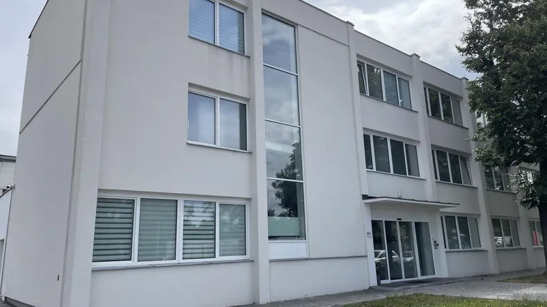 Modernes Bürogebäude mit großen Fenstern und Jalousien unter bewölktem Himmel.