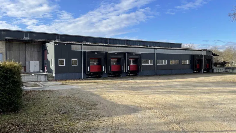 Großes Industriegebäude mit mehreren Laderampen und weitläufigem Vorplatz unter blauem Himmel.