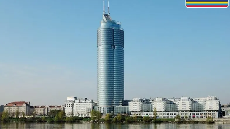 Moderne Glasfassade eines Hochhauses am Flussufer mit klarer Architektur und blauer Himmelskulisse.