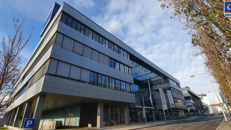 Modernes Bürogebäude mit mehreren Etagen und großen Fenstern unter einem bewölkten Himmel.