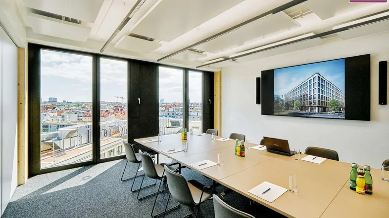 Moderner Konferenzraum mit großem Bildschirm, Teppichboden und weitem Stadtblick durch bodentiefe Fenster.