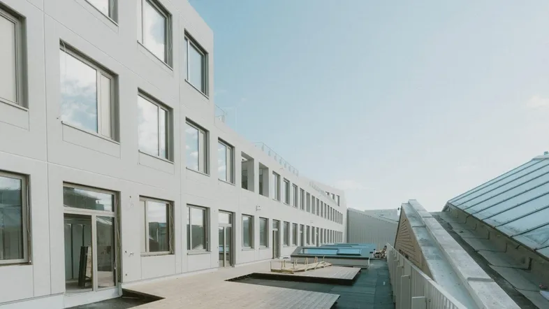 Moderne Gebäudefassade mit großen Fenstern und einer Holzterrasse im Außenbereich, ideal für Entspannung.