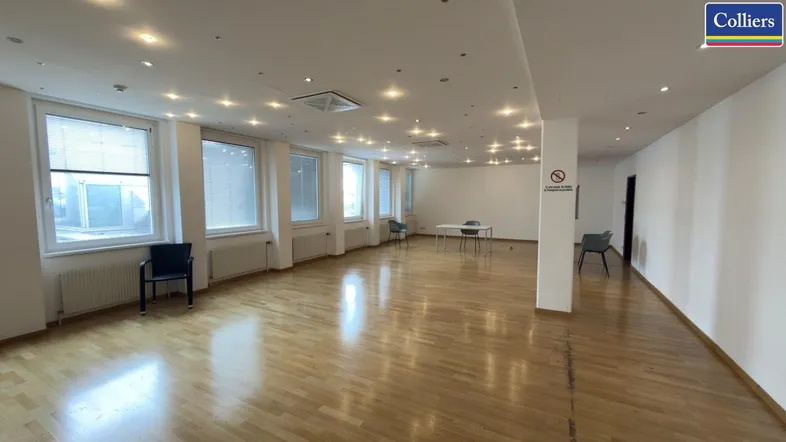 Großer, heller Büroraum mit Holzparkettboden, vielen Fenstern und moderner Deckenbeleuchtung.