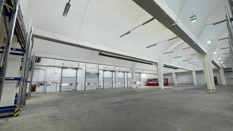 Geräumige Lagerhalle mit hohen Decken, Betonboden und mehreren Rolltoren für den Warenverkehr.