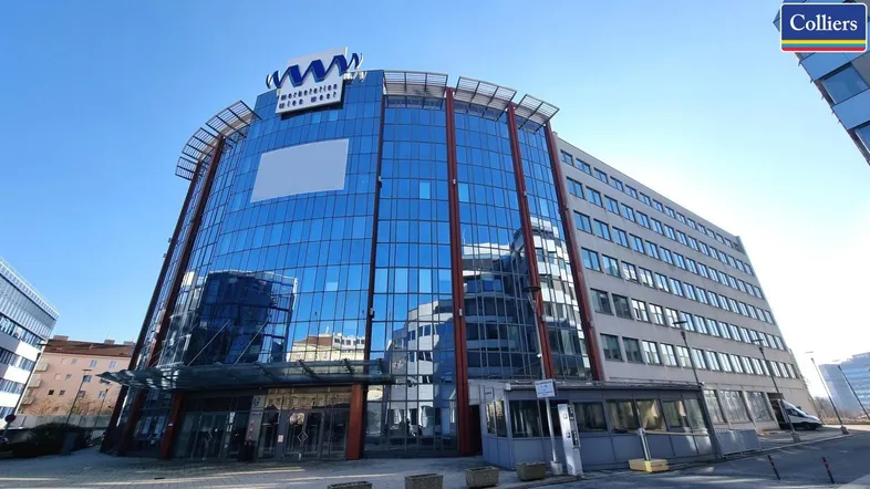 Modernes Bürogebäude mit auffälliger Glasfassade und blauer Beschriftung unter klarem Himmel.