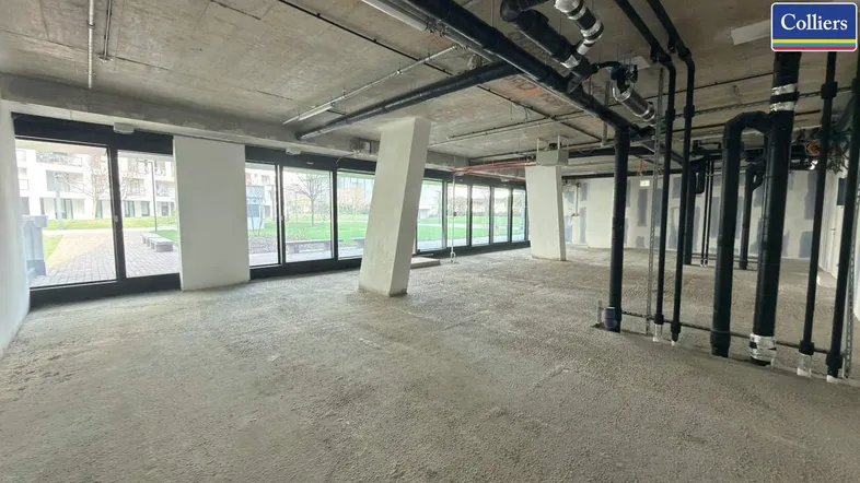 Großer, unfertiger Gewerberaum mit sichtbaren Installationen und großen Fenstern zum Außenbereich.