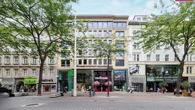 Moderne Geschäftsfassade an einer belebten Straße mit Geschäften und Bäumen, die das Gebäude säumen.