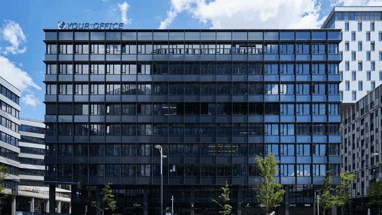 Modernes Bürogebäude mit großer Glasfassade und dem Schriftzug "YOUR OFFICE" unter blauem Himmel.
