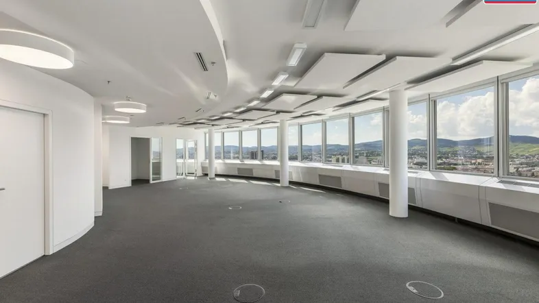 Großes, leeres Büro mit vielen Fenstern, die einen weiten Blick über die Stadt und Landschaft bieten.