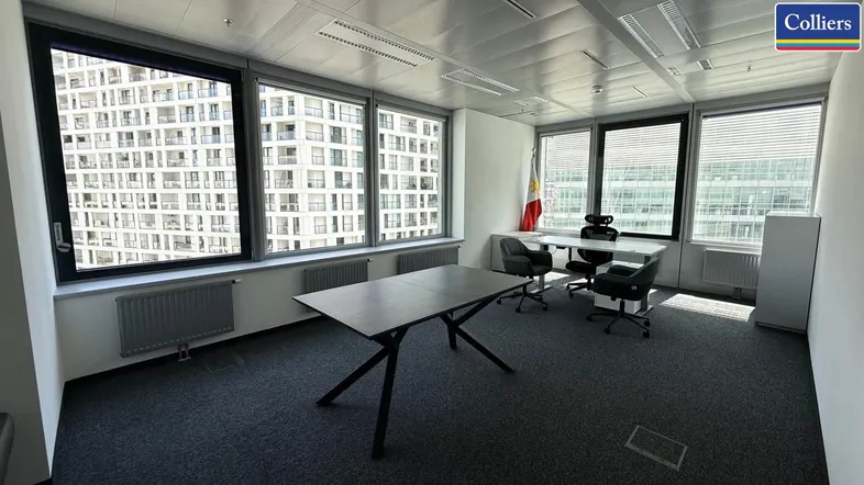 Modernes Büro mit großen Fenstern, Teppichboden und Blick auf umliegende Gebäude.