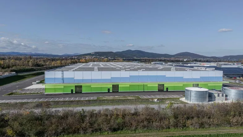 Großes, modernes Logistikzentrum mit farbiger Fassade in ländlicher Umgebung unter blauem Himmel.