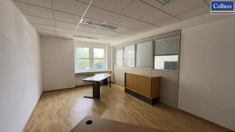 Helles Büro mit Holzfußboden, weißen Wänden und großen Fenstern, teilweise mit Trennwänden ausgestattet.