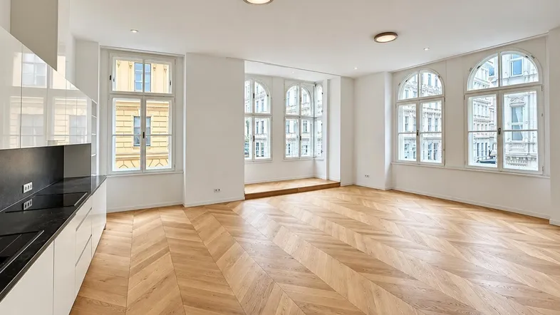Helles, offenes Wohnzimmer mit moderner Küche, Fischgrätparkett und großen Bogenfenstern.