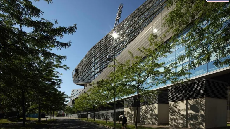 Modernes Gebäude mit markanter Architektur und Glasfassade, umgeben von Bäumen an einer Straße.