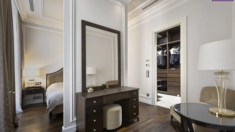 Elegantes Schlafzimmer mit dunklem Parkettboden, Schminktisch und Zugang zu einem begehbaren Kleiderschrank.
