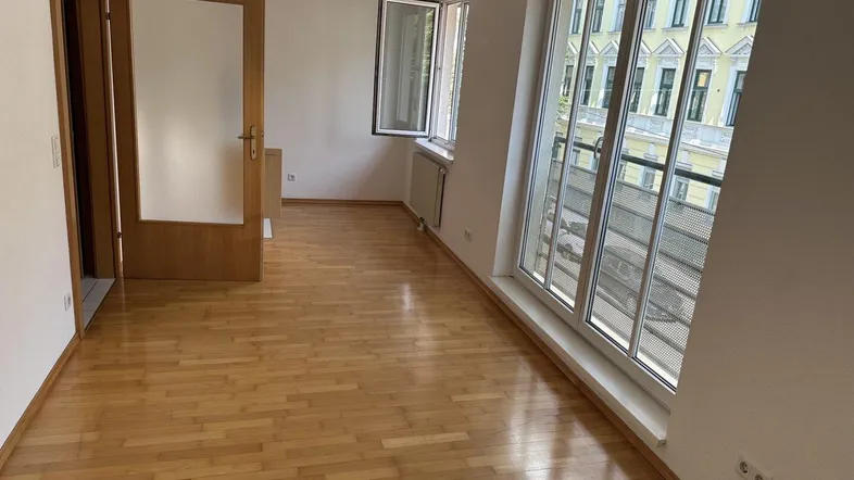 Helles Wohnzimmer mit Parkettboden, großen Fenstern und Zugang zu einem französischen Balkon.