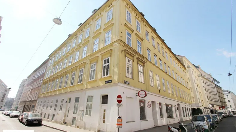 Historisches Eckgebäude mit gelber Fassade und vielen Fenstern in einer belebten Stadtstraße.