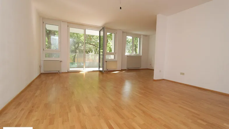 Helles Wohnzimmer mit Parkettboden, weißen Wänden und Zugang zu einem Außenbereich durch große Fenster.