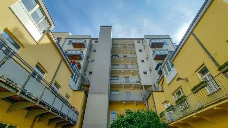 Blick in den Innenhof eines Wohnkomplexes mit mehreren Balkonen und einem zentralen Baum.