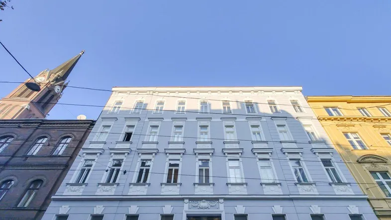 Historisches Gebäude mit blauer Fassade und hohen Fenstern, im Hintergrund ein Kirchturm.