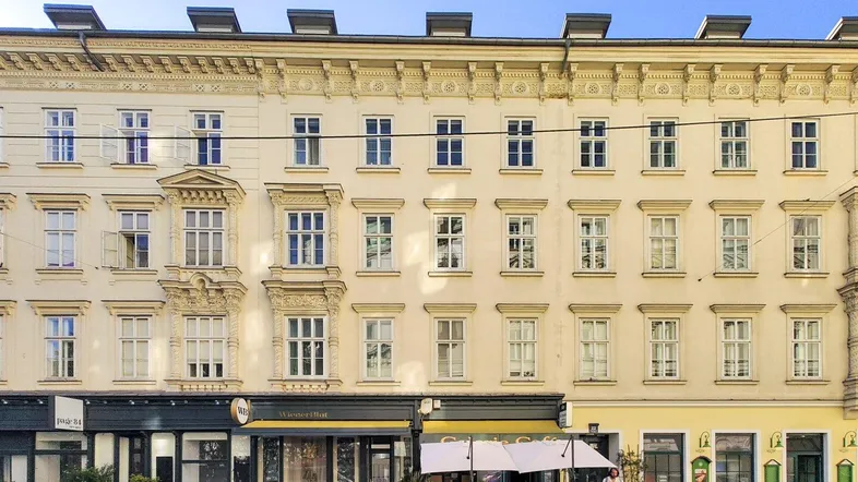 Klassische Fassade eines Wiener Altbaus mit Geschäften im Erdgeschoss und parkenden Autos.