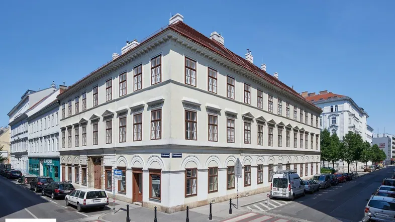 Historisches Eckgebäude in der Stadt mit vielen Fenstern und Geschäften im Erdgeschoss unter blauem Himmel.