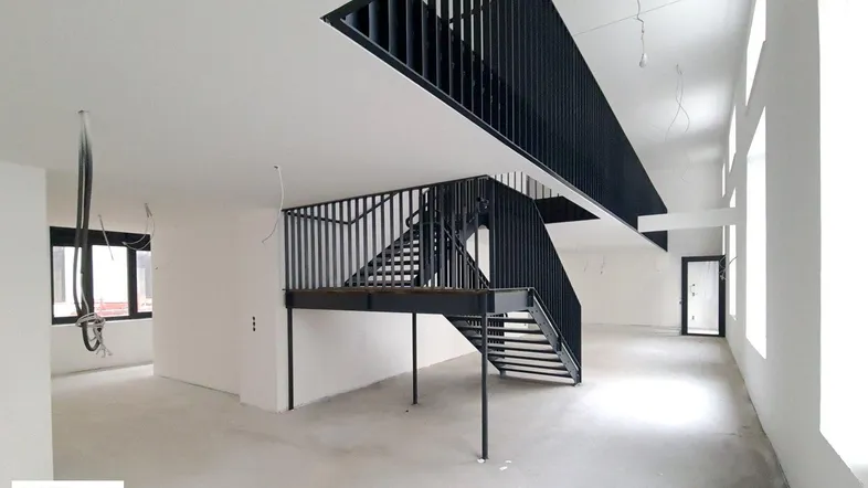 Großer, offener Innenraum im Rohbau mit moderner schwarzer Metalltreppe und hohen Decken.