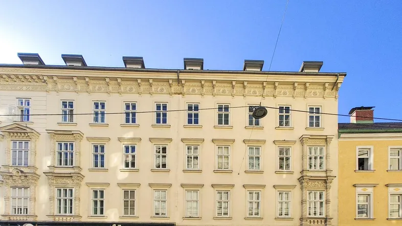 Historisches Gebäude mit reich verzierter Fassade, Erkerfenstern und Geschäften im Erdgeschoss unter blauem Himmel.