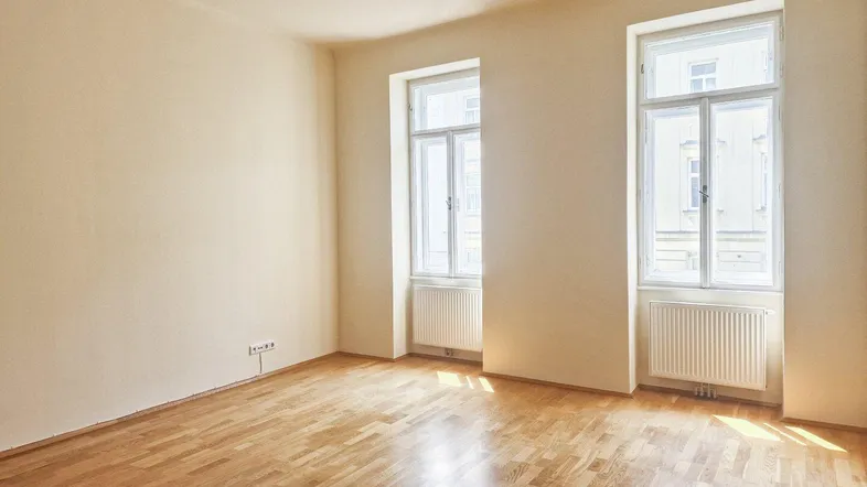 Helles Zimmer mit Parkettboden, hohen Fenstern und Heizkörpern, bereit zur individuellen Gestaltung.