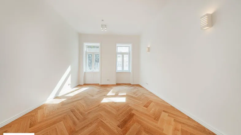Helles Wohnzimmer mit Fischgrätparkettboden und zwei großen Fenstern, die viel Tageslicht hereinlassen.