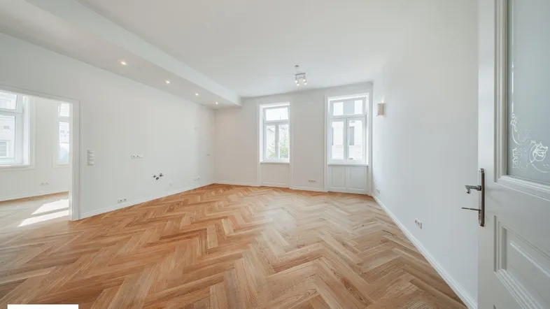 Helles, leeres Wohnzimmer mit Fischgrätparkett und hohen Fenstern, bereit zur individuellen Gestaltung.